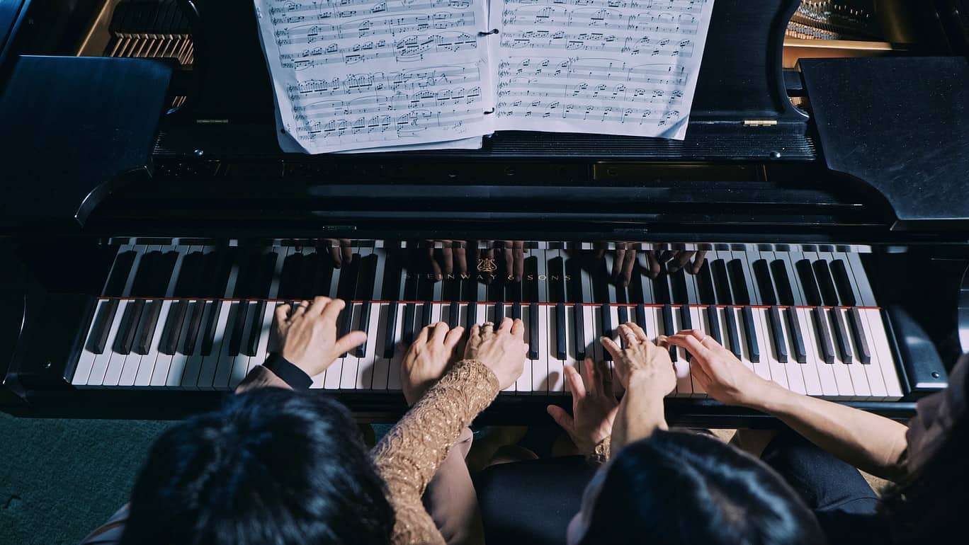 Top-down photo on a piano, two people playing the same piano together