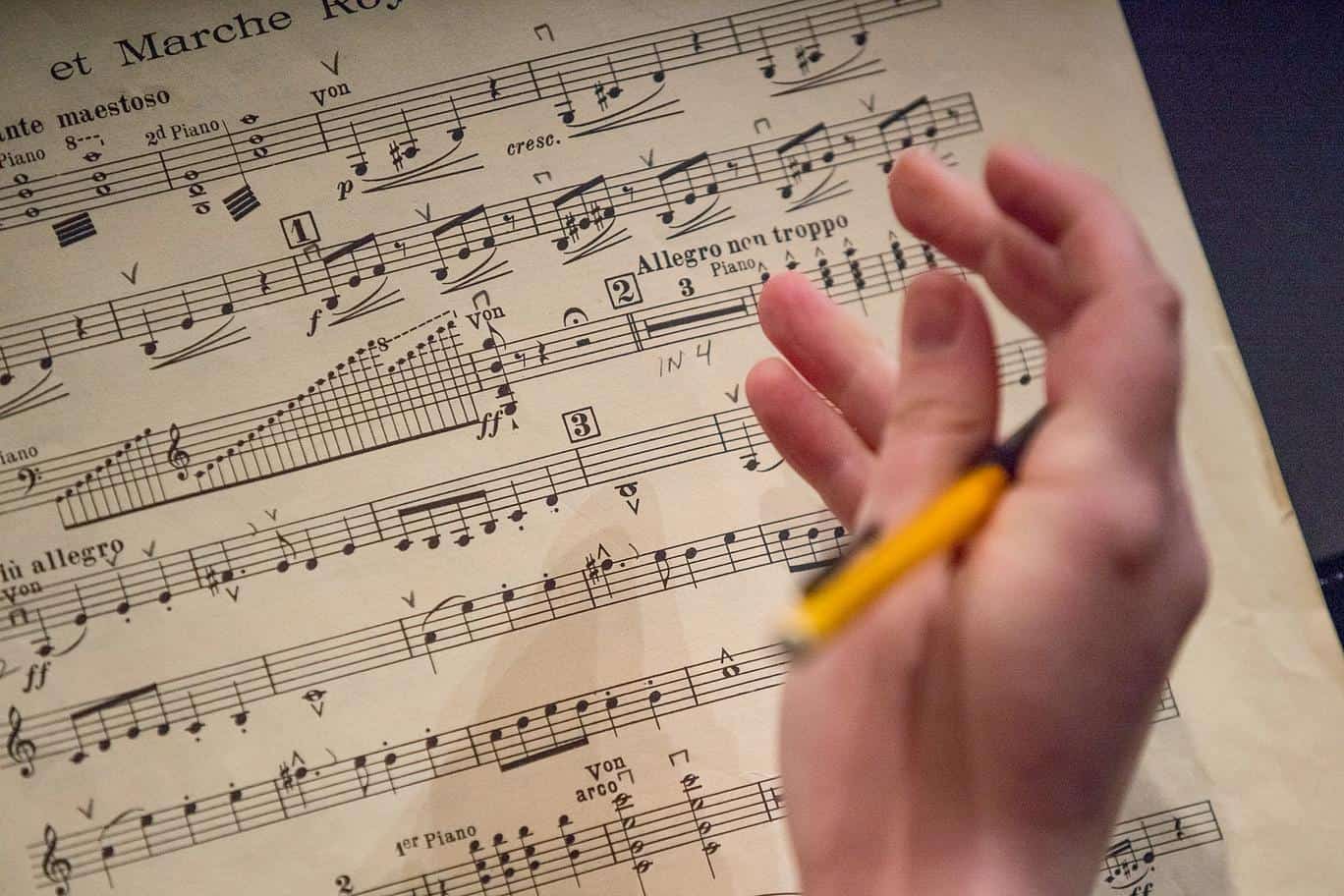 close up of a hand holding a pencil above sheet music, conducting