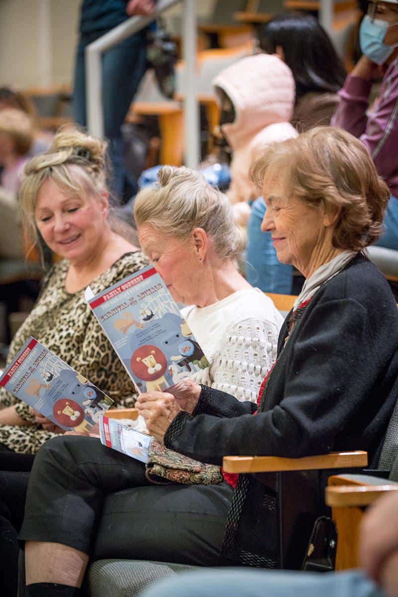 Three older women reading the concert program and smiling
