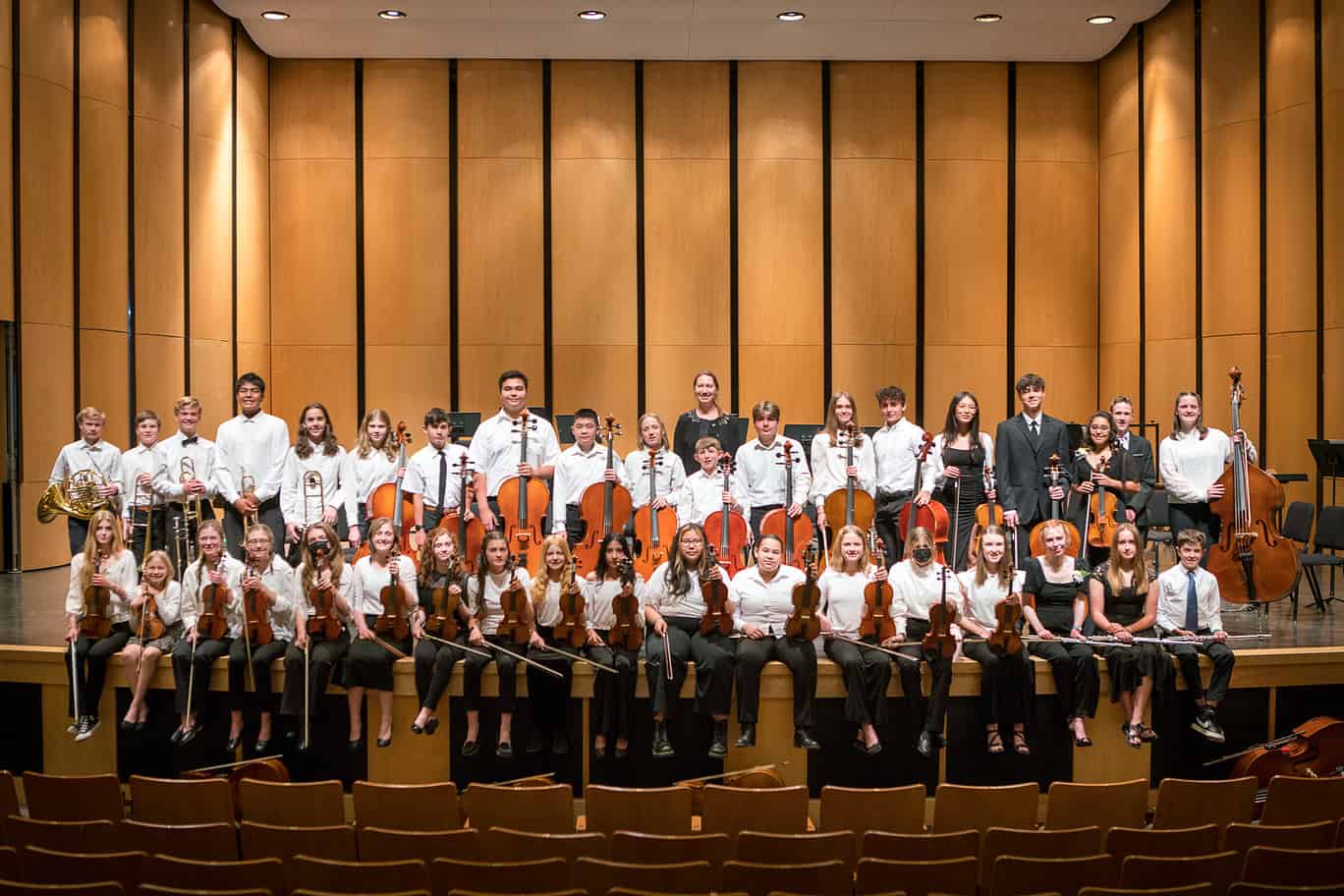 A large group of orchestra students posed for a portrait on stage