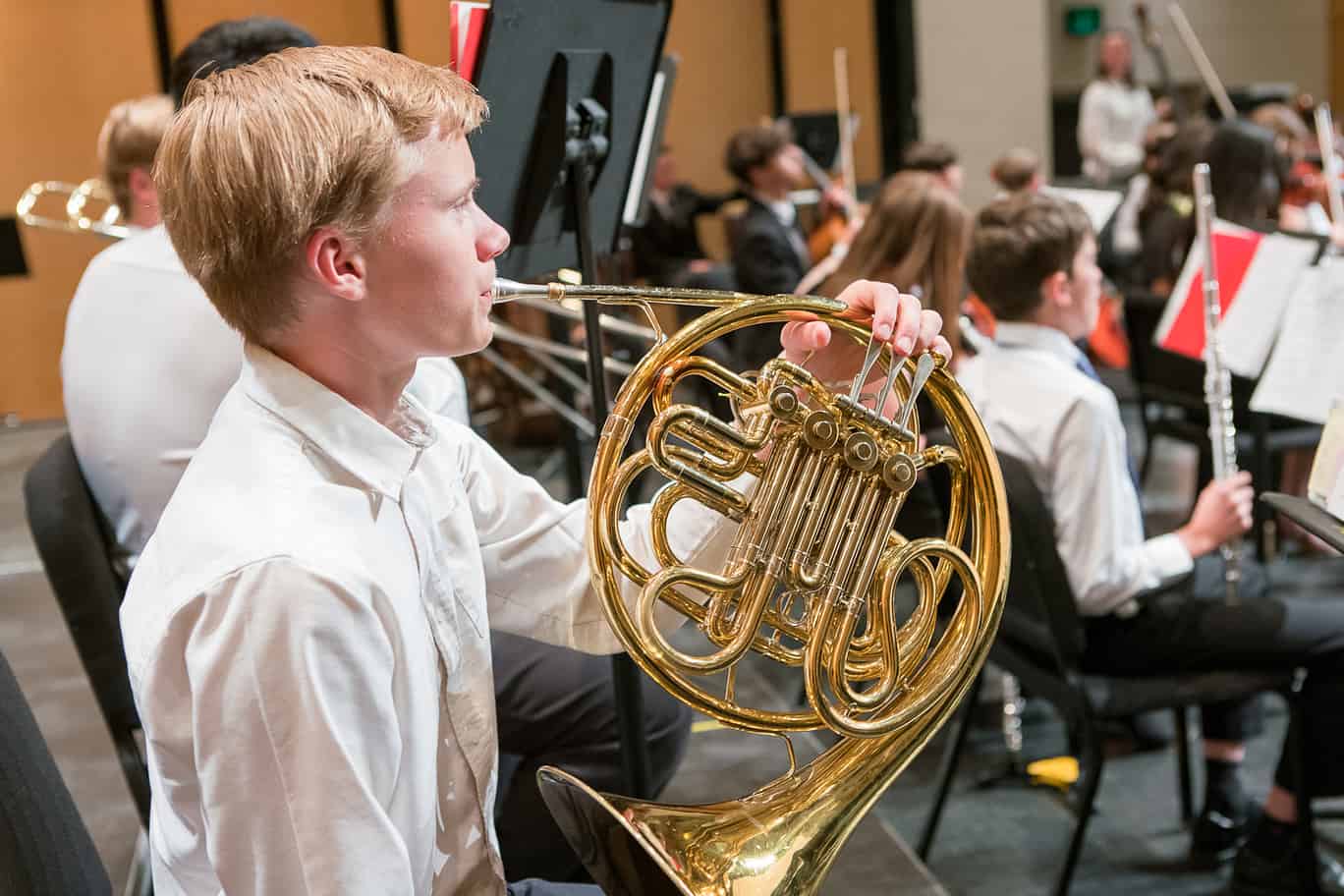 a young boy with blond hair plays french horn